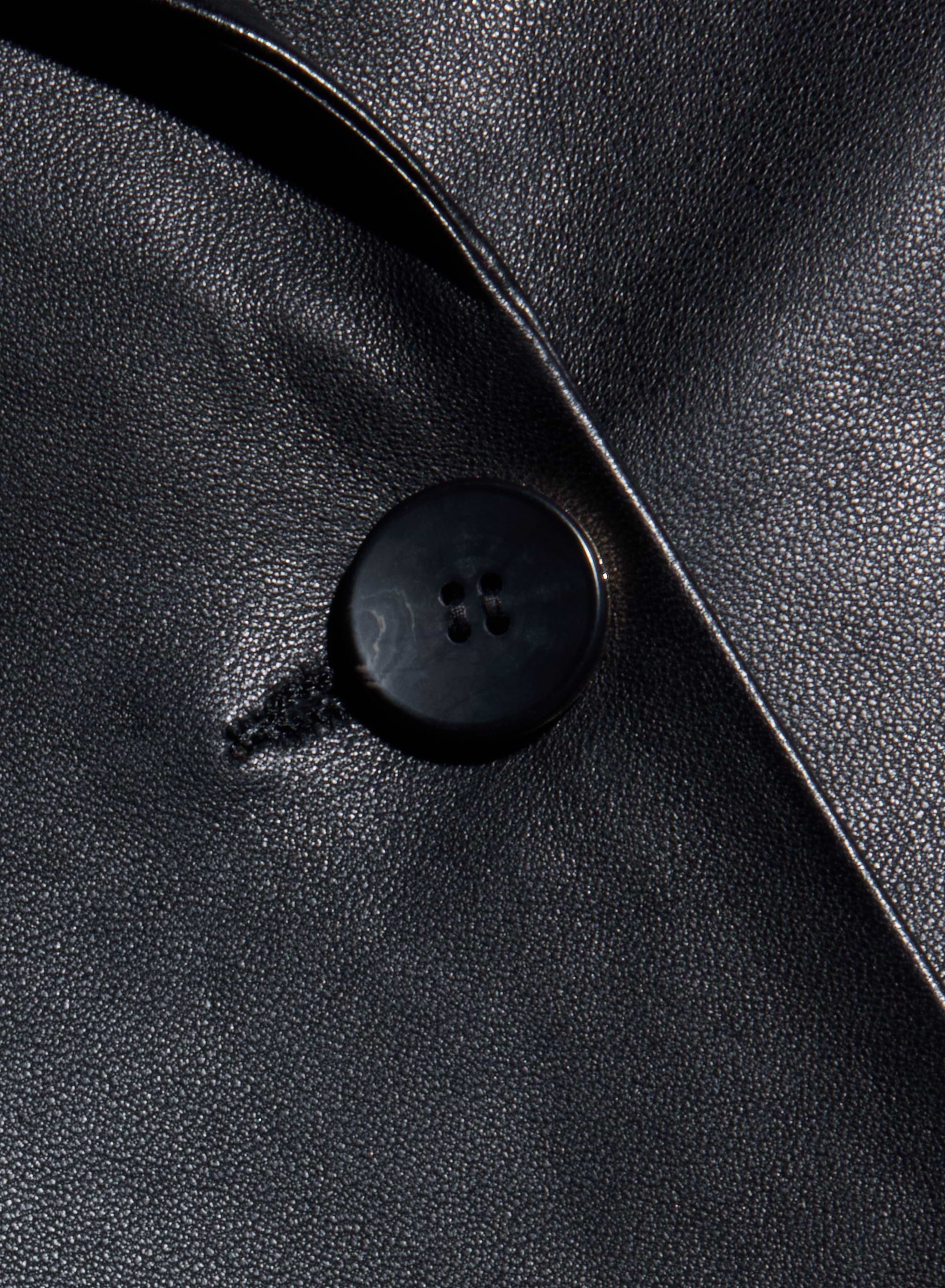Close-up of a black button sewn onto the shiny black leather fabric of the Chamberlain Leather Blazer, highlighting the texture and sheen of its lightweight leather and timeless, classic design.
