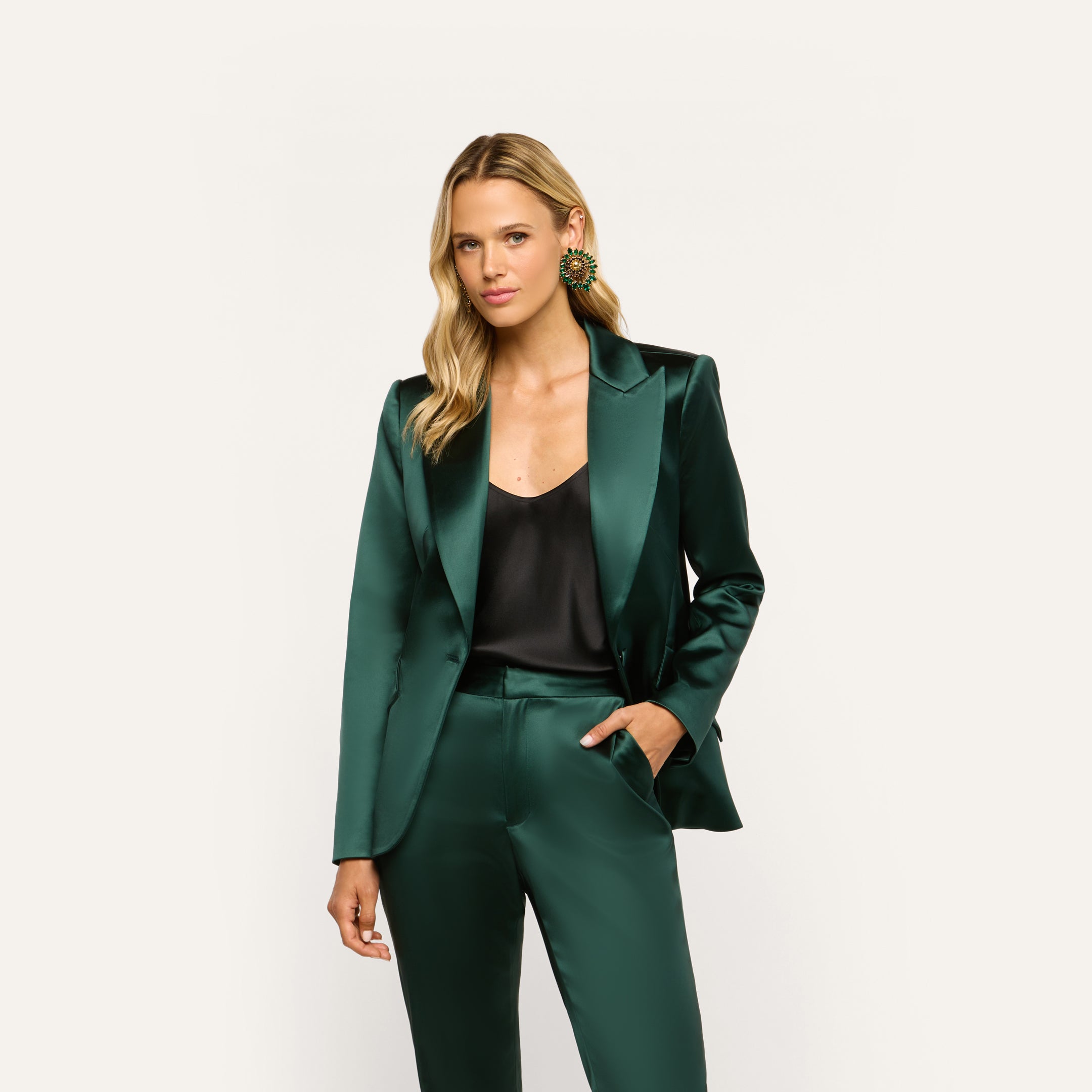 A person wearing a forest green Chamberlain Satin Blazer over a black camisole and matching stretch satin trousers.