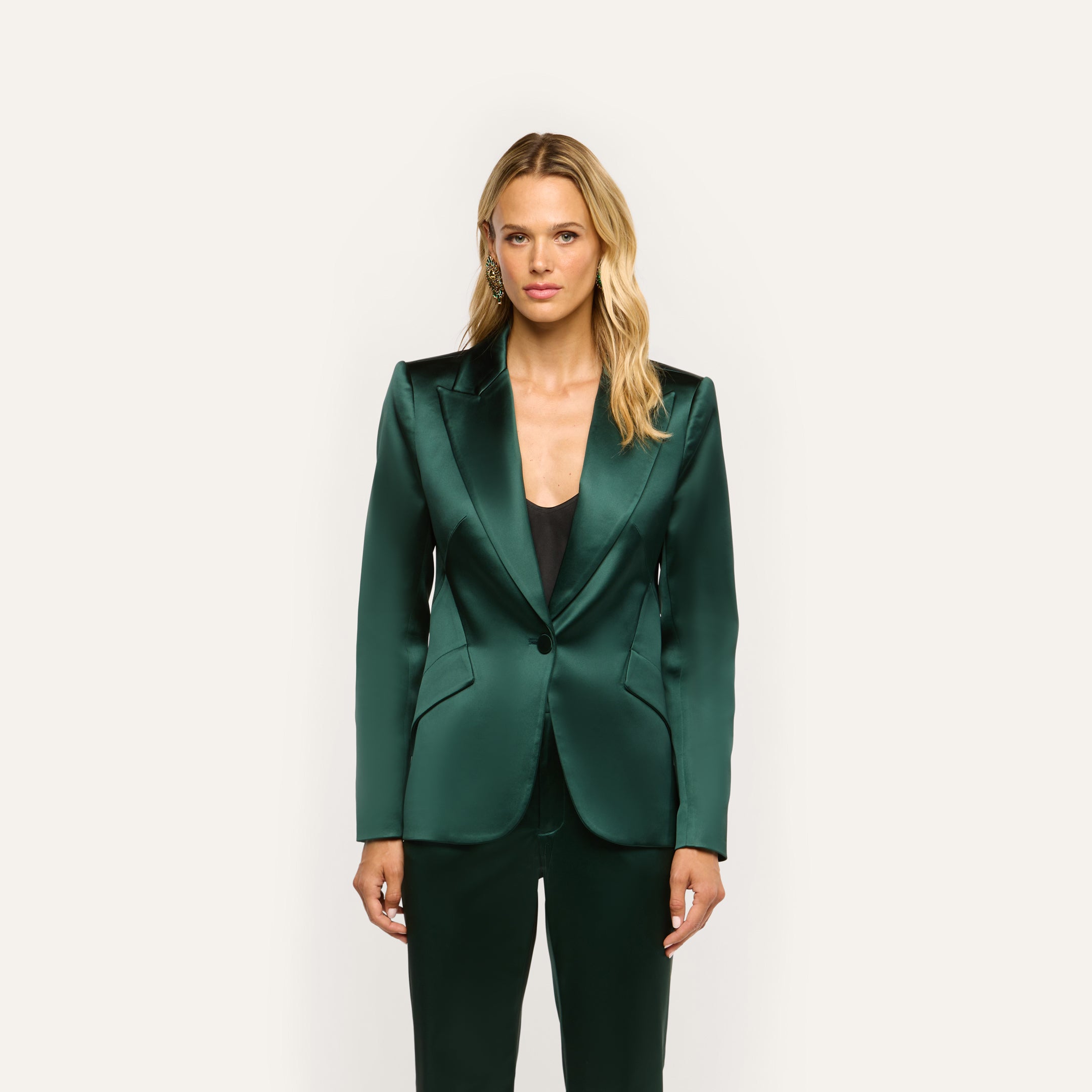 A woman wears a forest green Chamberlain Satin Blazer with sharp lapels over a black top.