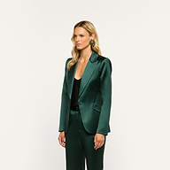 A person wearing a forest green Chamberlain Satin Blazer and matching trousers over a black top, accented with a large, round green and gold earring.