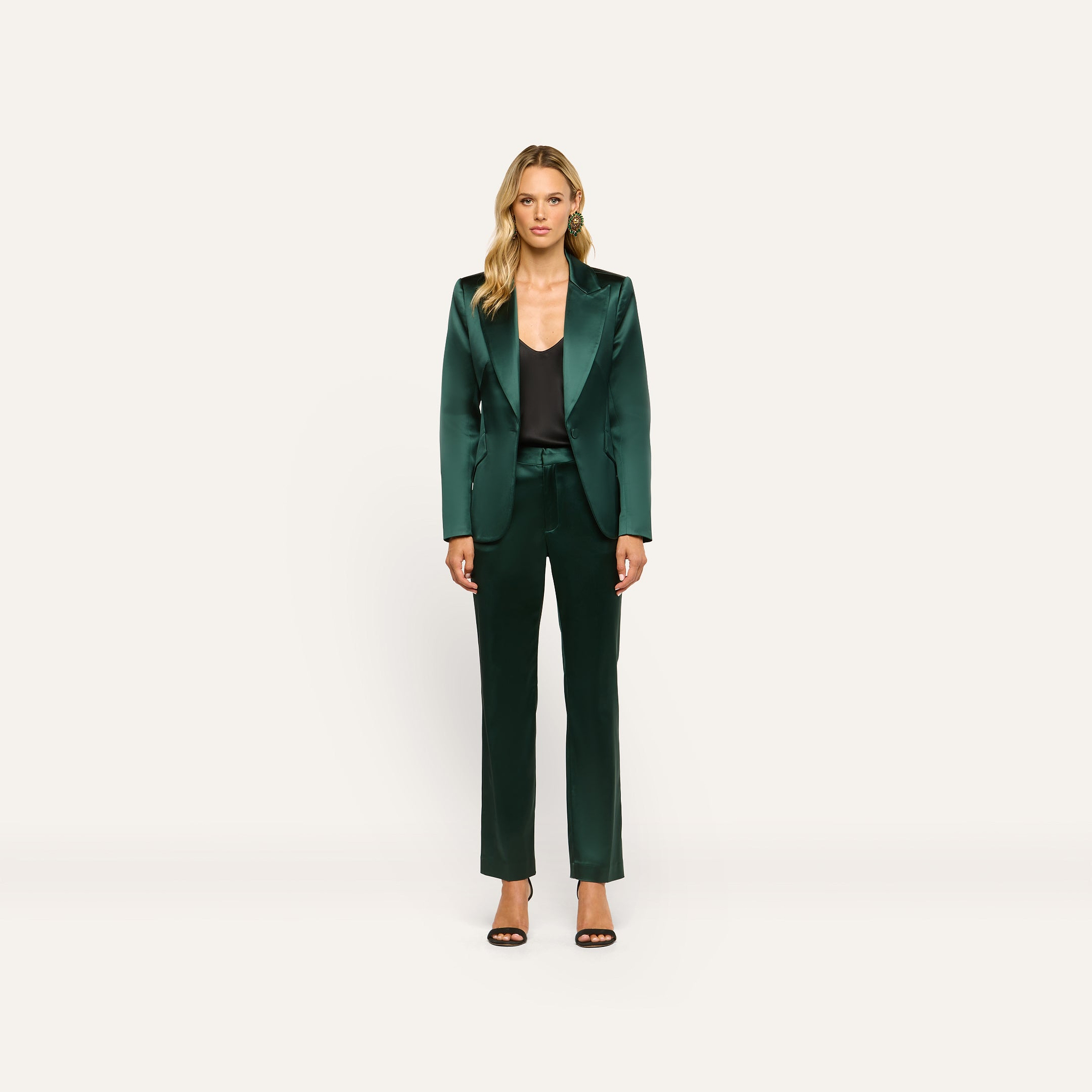 A woman wearing a forest green Chamberlain Satin Blazer and matching trousers over a black camisole, paired with black heeled sandals.