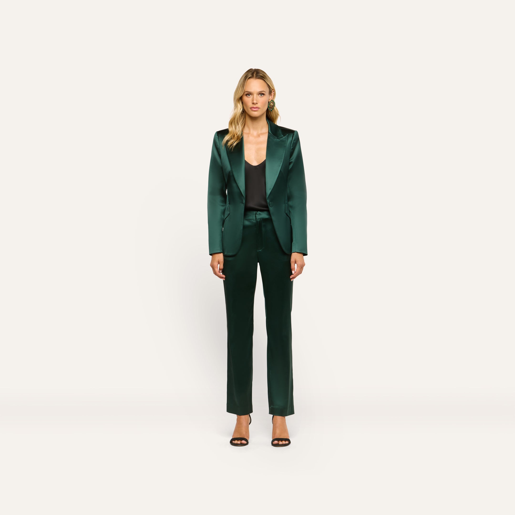 A woman wearing a forest green Chamberlain Satin Blazer and matching trousers over a black camisole, paired with black heeled sandals.