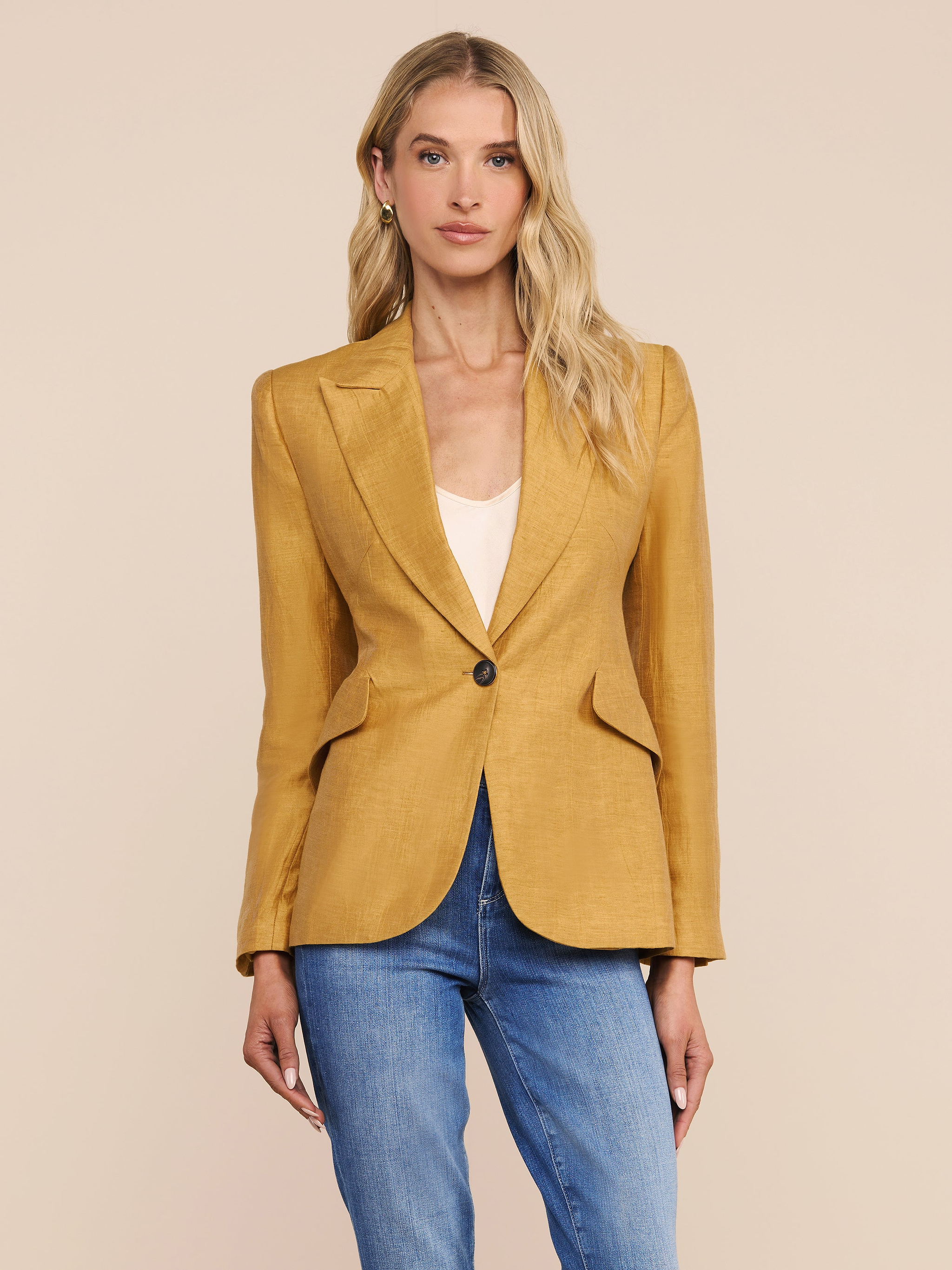 A woman stands facing forward against a plain, light background, wearing the Chamberlain Linen-Blend Blazer in mustard yellow over a white top and blue jeans.