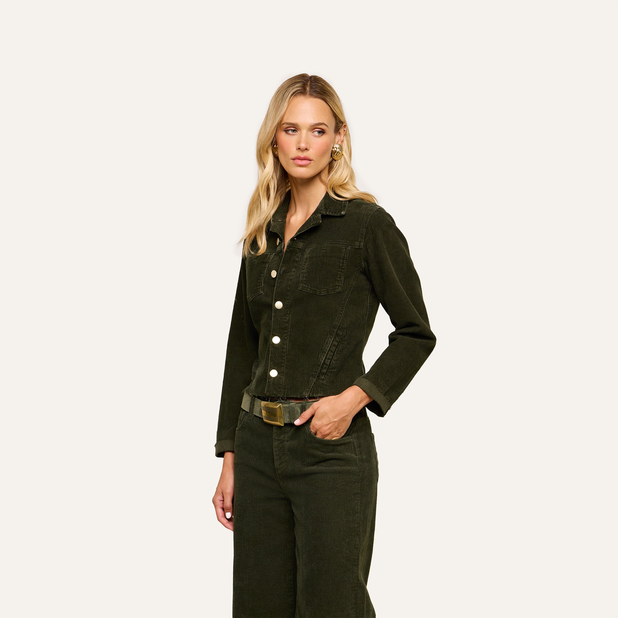 A woman with long blonde hair wears the Janelle Corduroy Jacket and matching pants, posing with one hand in her pocket against a plain light background.