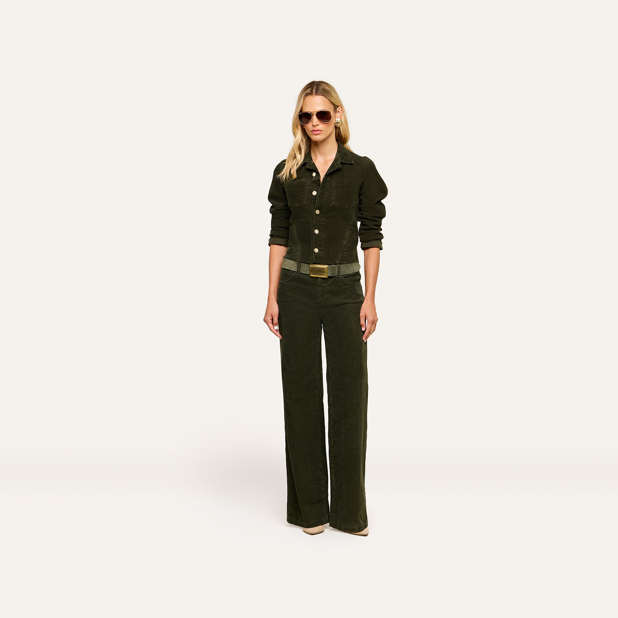 A person wearing sunglasses, a dark long-sleeve button-up shirt, and matching wide-leg pants stands facing forward on a plain light background, layered with the Janelle Corduroy Jacket.