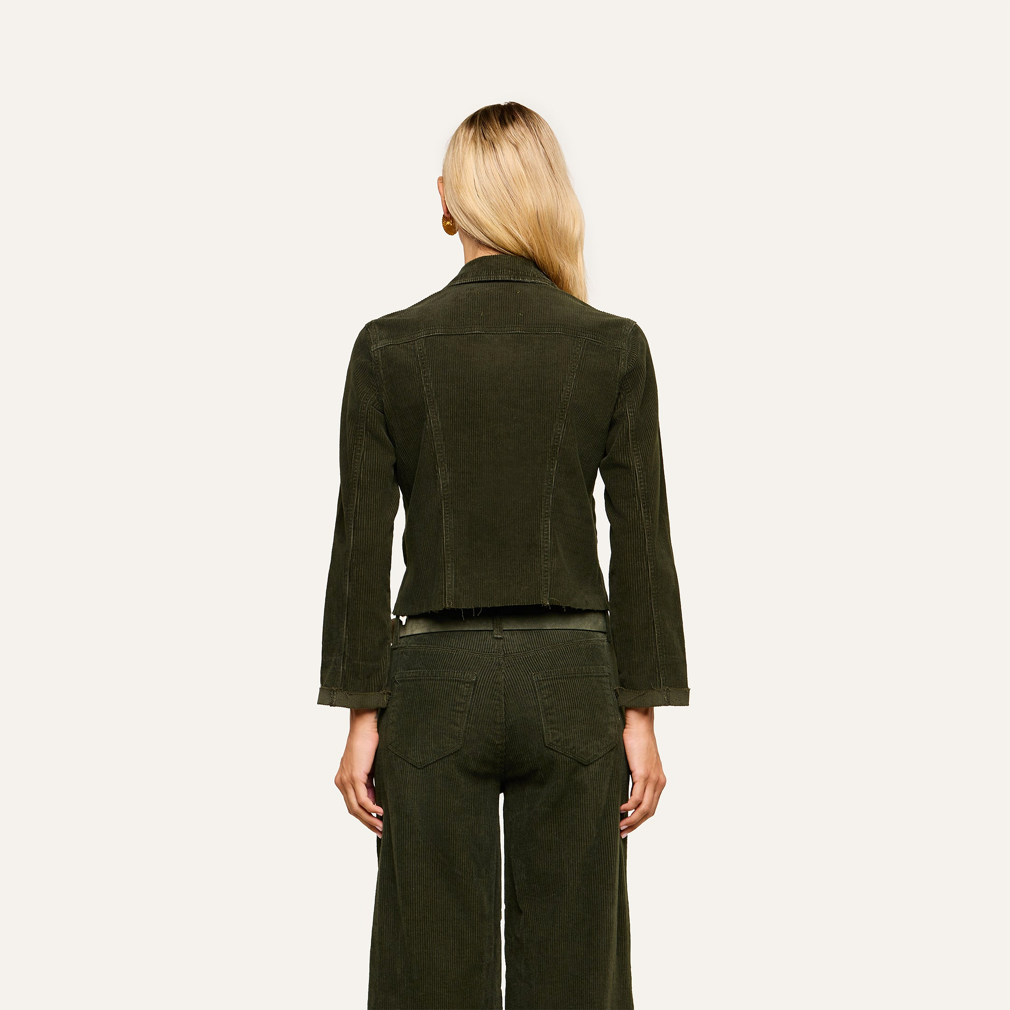 A person with long blonde hair, seen from behind, wears the Janelle Corduroy Jacket in green along with matching pants against a plain light background.