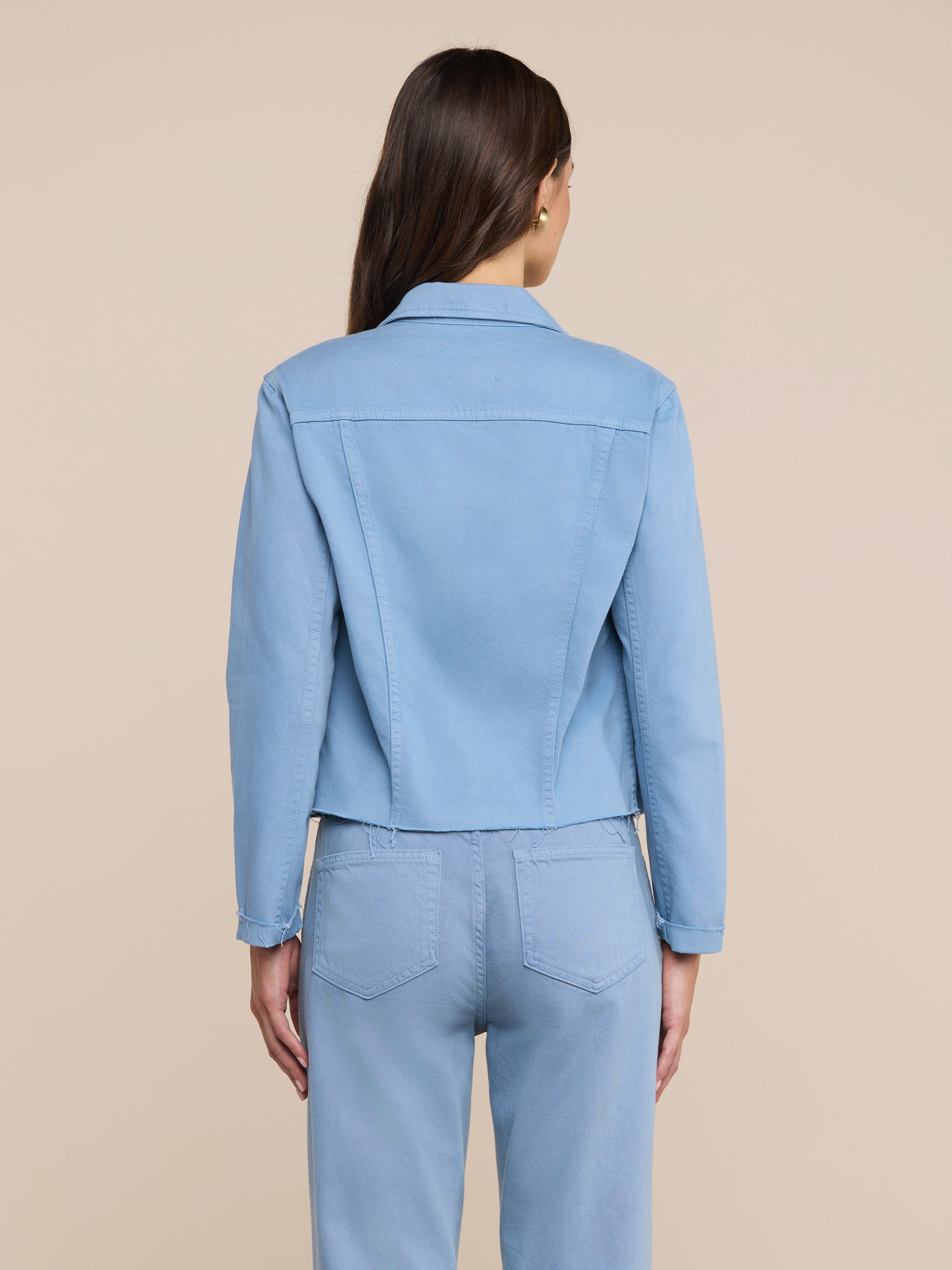 Modella ripresa di schiena, con indosso una giacca Janelle dal taglio aderente in denim azzurro e jeans abbinati.