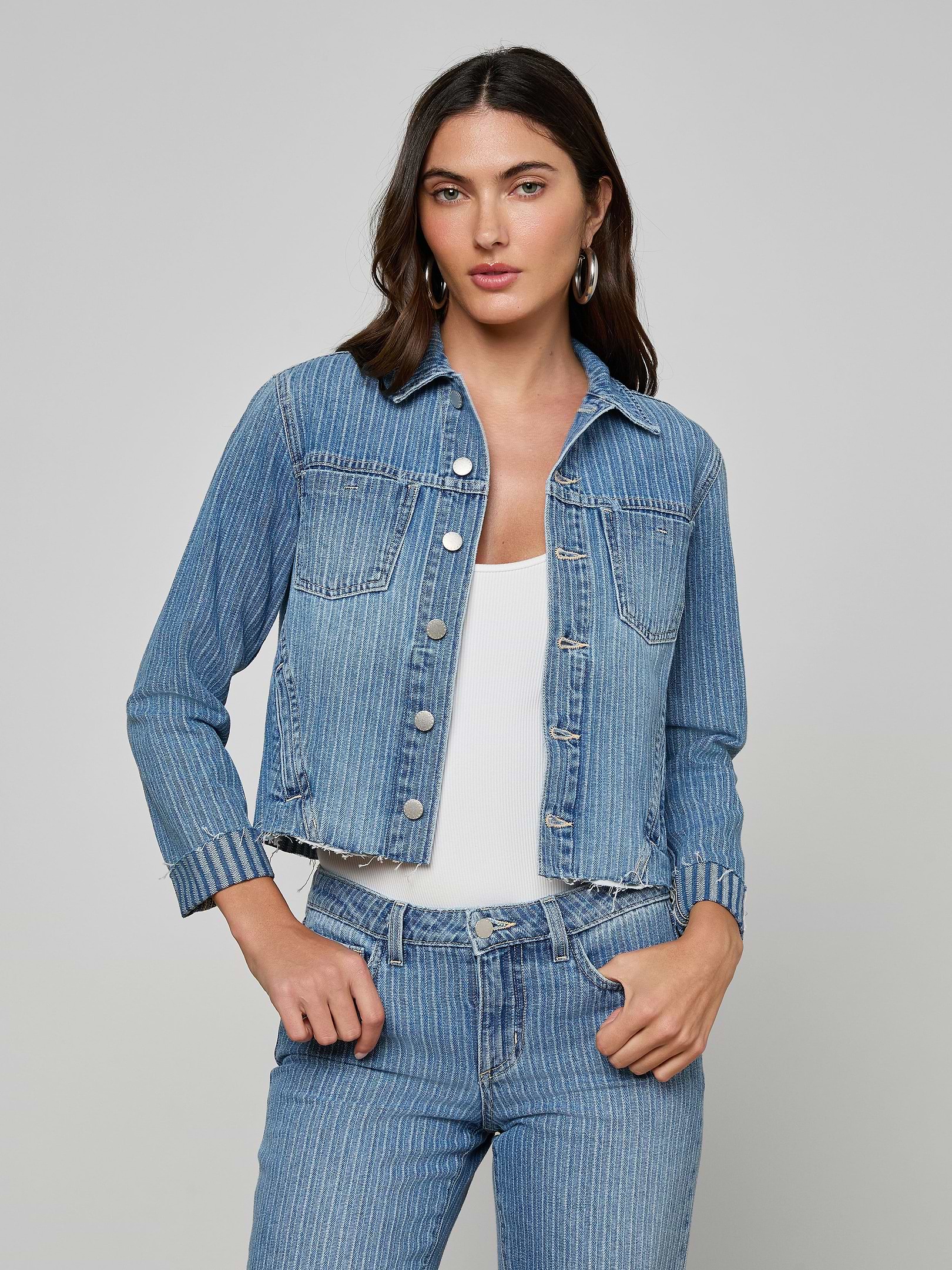 A woman wears the slim-fit Janelle Jean Jacket in all-cotton pinstriped indigo over a white top, paired with matching pinstriped jeans, standing against a plain light background.