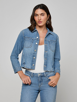A person wears the Janelle Jean Jacket, a slim fit pinstriped denim piece, over a white ribbed top with matching jeans against a light gray background.