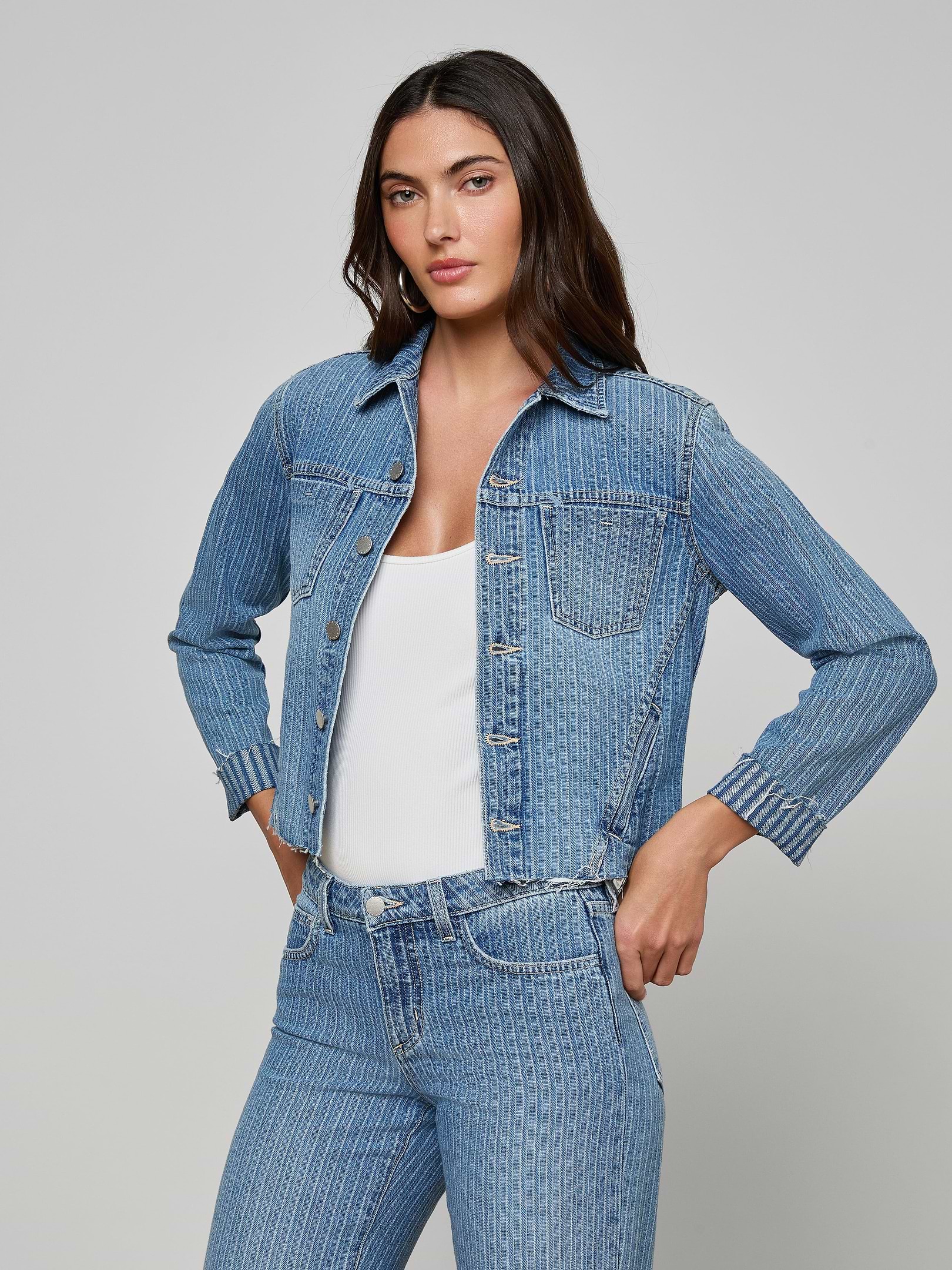 A woman stands with her hands in her pockets, wearing the slim fit Janelle Jean Jacket and matching all-cotton denim jeans over a white top, looking forward against a plain light background.