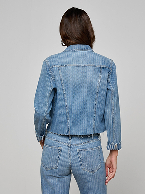 A person with long brown hair is seen from behind, wearing the Janelle Jean Jacket in light blue pinstriped denim with matching high-waisted jeans against a plain light gray background.