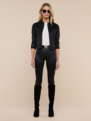 A woman stands facing forward in sunglasses, the Janelle Coated Jean Jacket, a white top, black fitted pants, and knee-high black boots against a plain beige background.