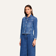 A woman stands facing forward, wearing the Janelle Jean Jacket in a medium wash with front pockets and a slim fit, paired with matching wide-leg blue jeans against a plain light background.