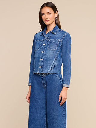 Wearing the Janelle Jean Jacket and matching wide-leg jeans in a medium wash, a woman stands against a plain beige background and looks at the camera with a neutral expression.
