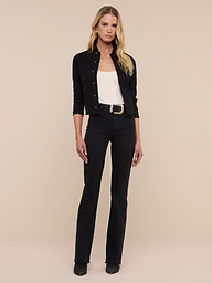 A woman with long blonde hair stands against a beige background, wearing the Janelle Jean Jacket over a white top, paired with black high-waisted jeans, a belt, and black heeled shoes. She looks at the camera with a neutral expression.