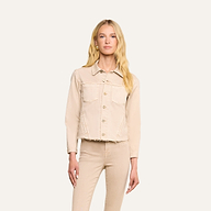 Une femme aux longs cheveux blonds porte la veste « Janelle Jean » et le pantalon assorti, de couleur beige avoine, dans une coupe féminine. Elle se tient debout, face à lobjectif, devant un fond beige uni, une main le long du corps et le visage impassible.