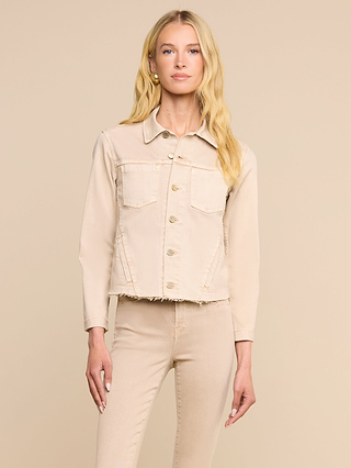 Eine Frau mit langen blonden Haaren trägt die Janelle-Jeansjacke und die dazu passende Hose in der Farbe „Oatmeal-Beige“, die in einer femininen Passform geschnitten sind. Sie steht mit dem Blick nach vorne vor einem schlichten beigen Hintergrund, eine Hand an der Seite und mit neutralem Gesichtsausdruck.