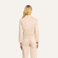 Une femme aux longs cheveux blonds, de dos, porte la veste « Janelle Jean » de couleur beige avoine, assortie à un pantalon en denim stretch de la même teinte, sur un fond beige uni.