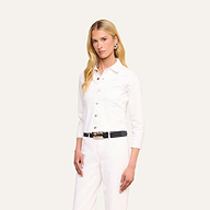 Una donna dai lunghi capelli biondi indossa la giacca Janelle Jean in una versione femminile in denim bianco, abbinata a pantaloni bianchi coordinati e a una cintura nera, mentre posa su uno sfondo beige a tinta unita.
