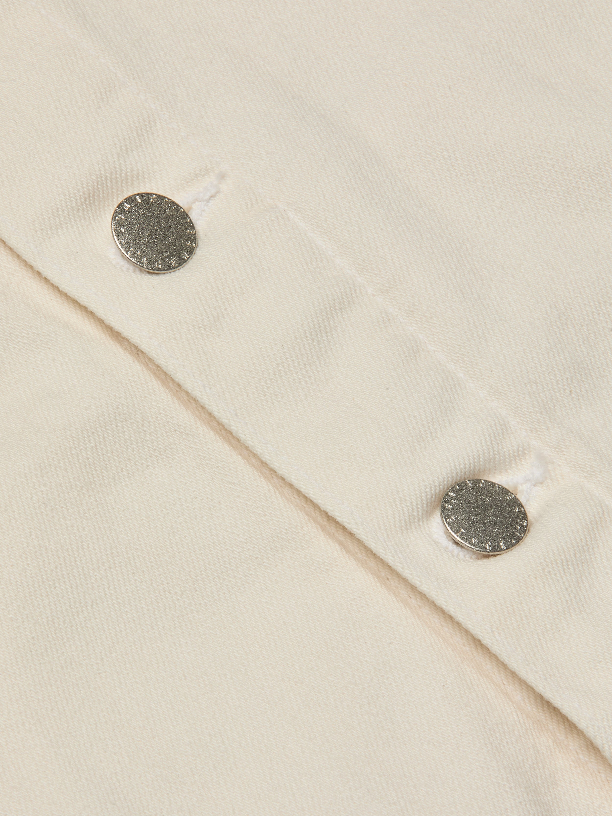 Close-up of two silver snap buttons on light beige fabric, likely from the Janelle Jean Jacket, with visible stitching and textured detail.