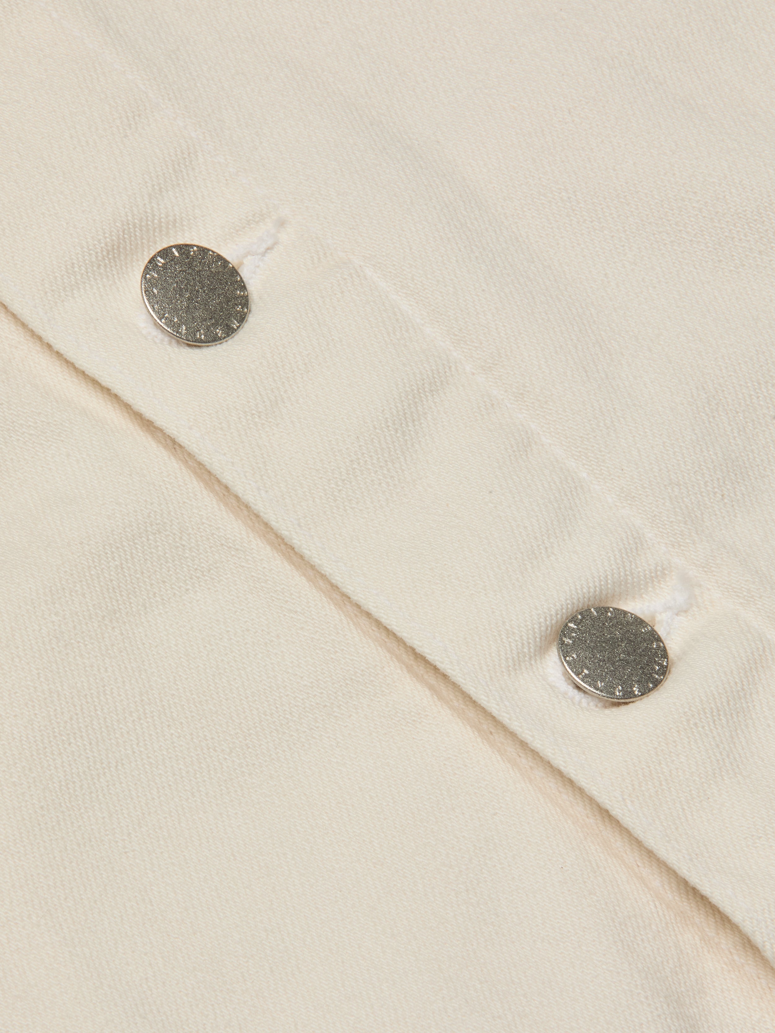 Close-up of two silver snap buttons on light beige fabric, likely from the Janelle Jean Jacket, with visible stitching and textured detail.
