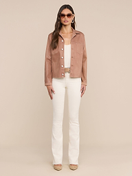 A woman stands facing forward against a plain white background, wearing sunglasses, the Janelle Coated Jean Jacket in hazelnut brown, a cream top, cream bell-bottom pants, and beige heels.