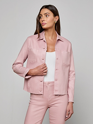 A woman wearing the Janelle Coated Jean Jacket in light pink with matching slim fit pants over a white top stands against a plain light background, looking to her left with one hand by her side and the other on her hip.