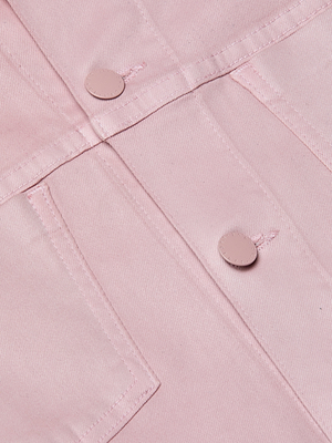 Close-up of the Janelle Coated Jean Jacket in light pink, featuring two flap pockets and round pink front buttons. The coated denim highlights visible fabric texture and stitching for a stylish leather-like look.