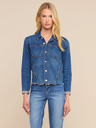 Indossando la giacca “Janelle Jean” dal taglio femminile e jeans in denim elasticizzato abbinati, una persona dai lunghi capelli biondi è in posa su uno sfondo beige neutro.
