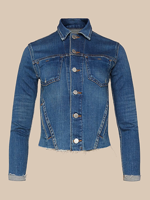 The Janelle Jean Jacket is a blue stretch denim piece with silver buttons, a feminine fit, two front chest pockets, a raw hem, long sleeves, and visible seam details, shown against a plain beige background.