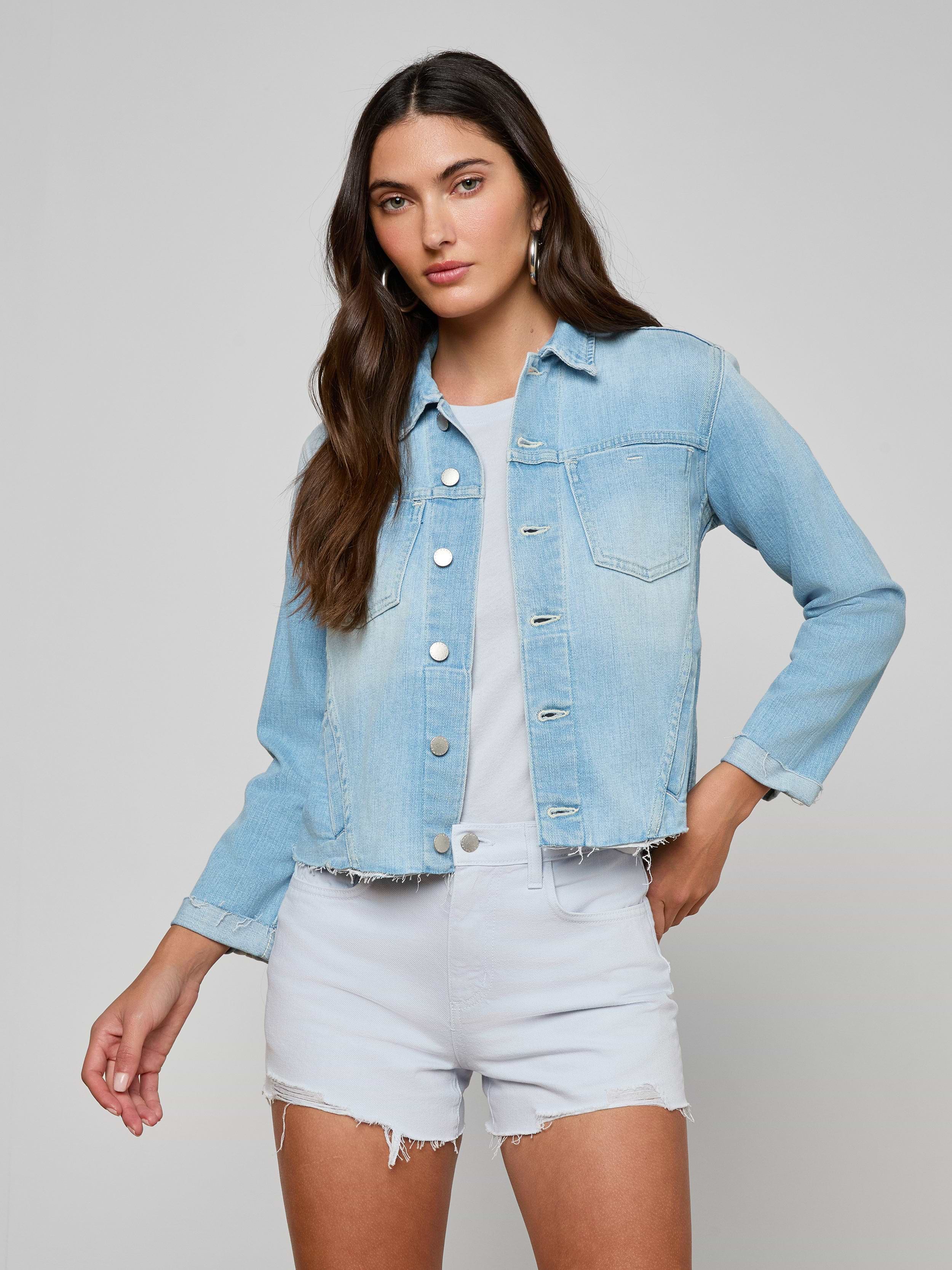 Wearing the Janelle Jean Jacket over a white shirt and matching denim shorts, a woman stands with one hand on her hip against a plain background.
