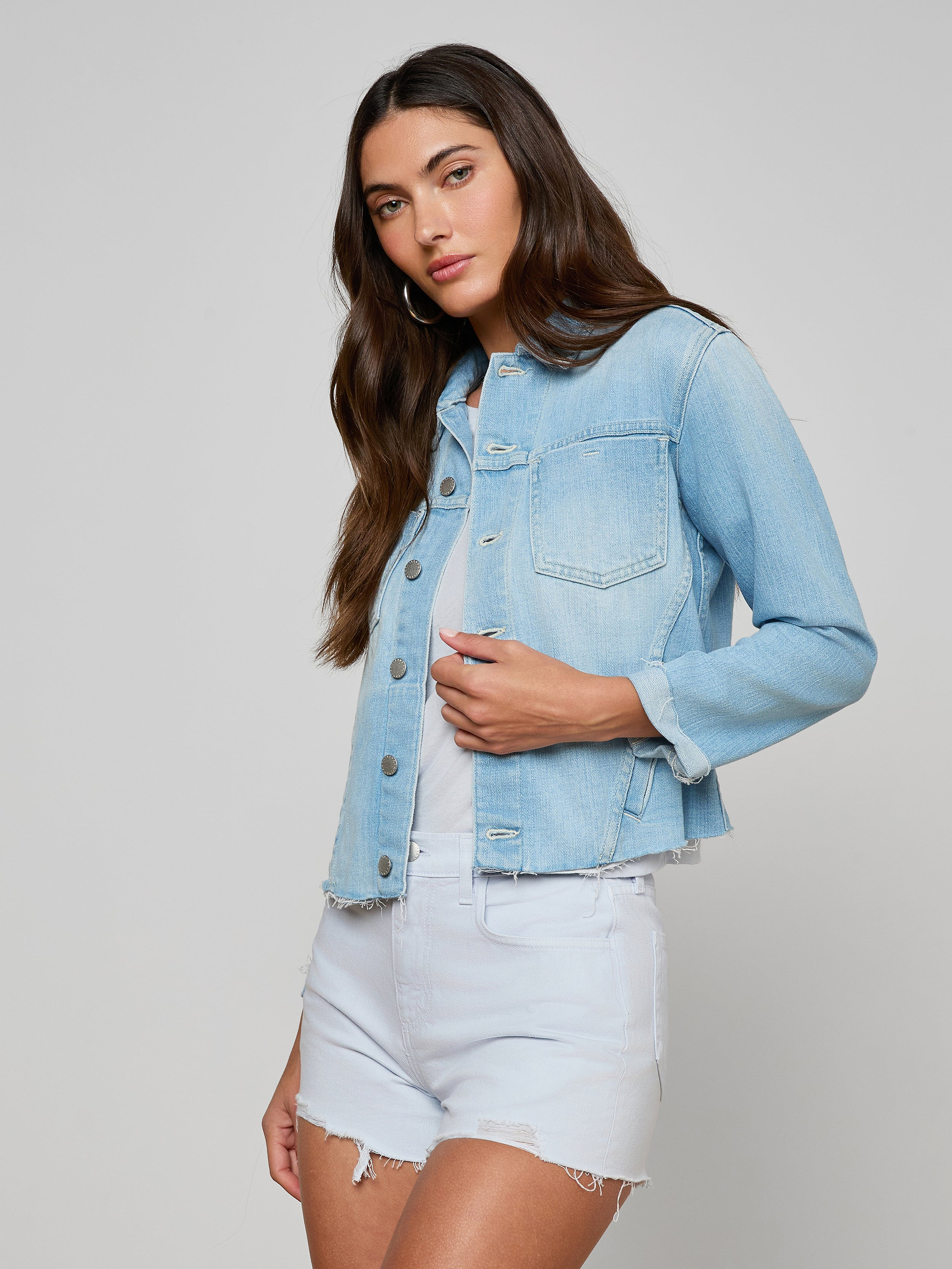 Wearing the Janelle Jean Jacket over a white shirt and light denim shorts, a woman with long brown hair stands against a plain off-white background.