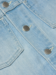Close-up of light blue denim fabric with visible stitching and two metallic buttons, likely part of a pocket on the Janelle Jean Jacket.