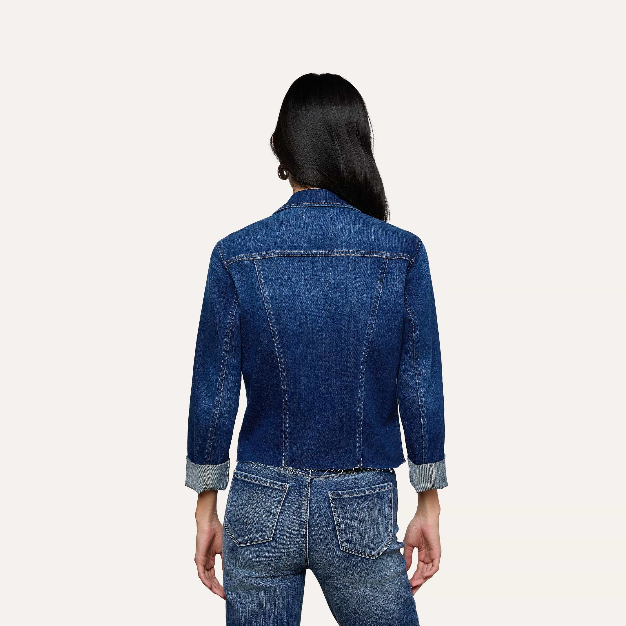 A person with long dark hair is shown from the back, wearing the Janelle Jean Jacket with rolled sleeves and matching blue denim jeans against a plain light background.