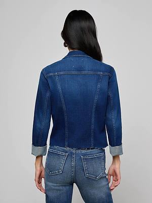 A person with long dark hair, seen from behind, wears the Janelle Jean Jacket—an indigo denim piece with a slim fit and 3/4 sleeves—paired with matching blue jeans against a plain gray background.