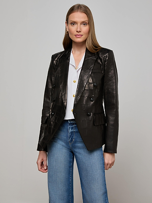 A woman with long straight hair wears the Kenzie Leather Blazer in black croc-embossed leather over a white button-up shirt and blue jeans, standing against a plain light gray background with a neutral expression.
