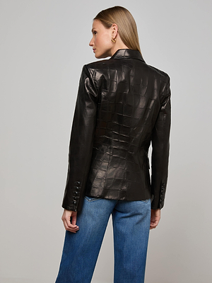 A woman with straight blonde hair models the Kenzie Leather Blazer—black and croc-embossed—paired with blue jeans, her back facing the camera against a plain light gray background.