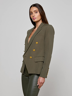 A woman with long brown hair models the L'AGENCE Kenzie Double-Breasted Blazer in ribbed olive with gold buttons and matching pants, standing against a plain light gray background.