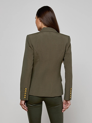 A woman with long brown hair is shown from the back, wearing L'AGENCE's Kenzie Double-Breasted Blazer in ribbed olive with gold sleeve buttons and matching pants, standing against a plain light gray background.