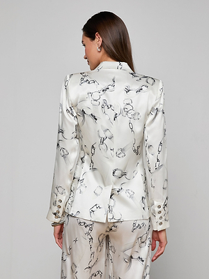 A woman with brown hair is seen from behind wearing the Colin Silk Blazer, a double-breasted white silk charmeuse jacket with a black abstract pattern, gold sleeve buttons, and a back slit.