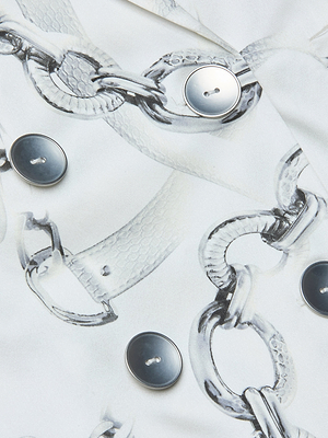 Close-up of the Colin Silk Blazer, featuring silk charmeuse fabric with a printed silver chain and buckle pattern, accented by shiny round metallic buttons on its double-breasted design.