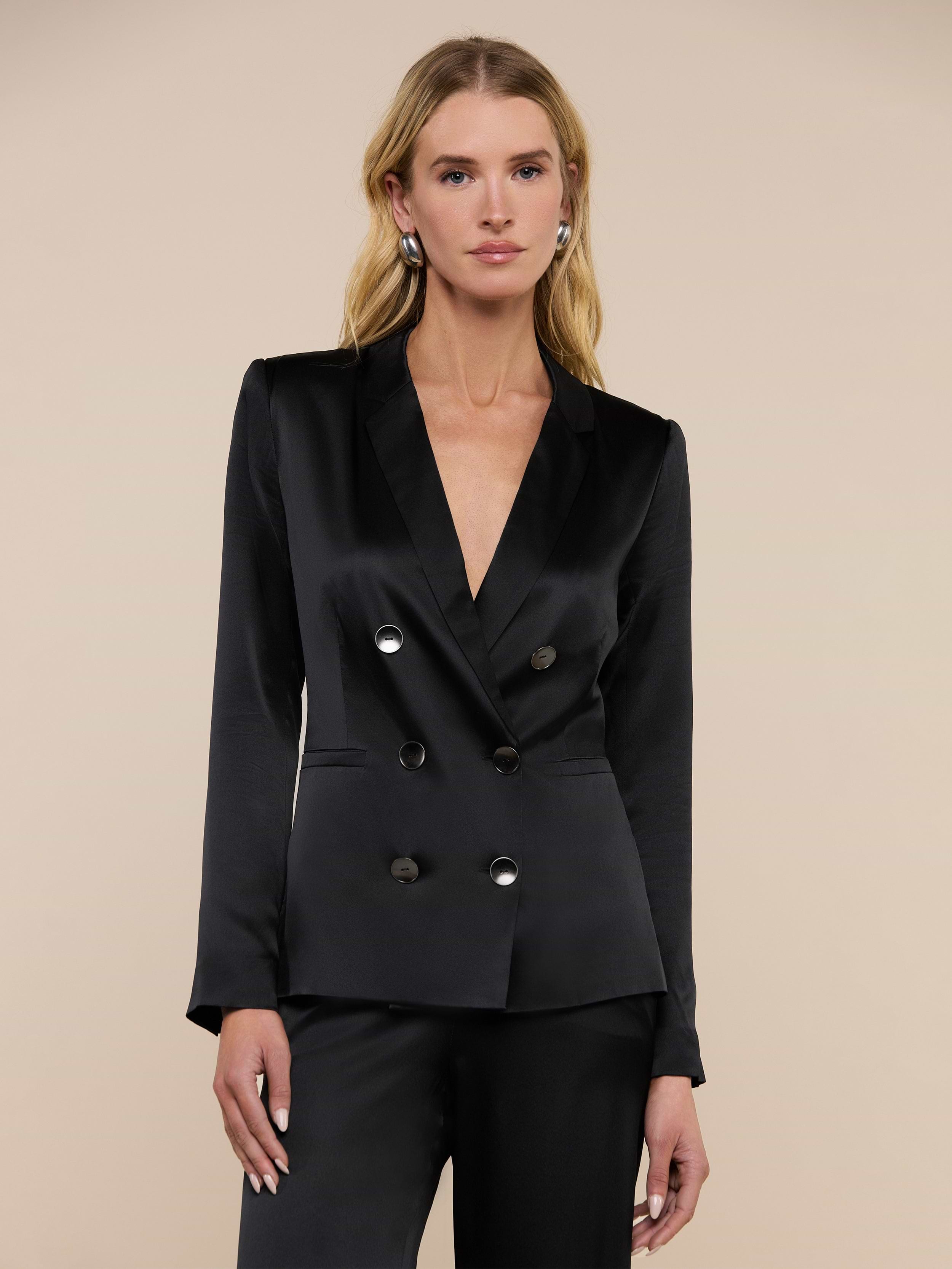 A woman stands against a plain light background, looking forward with a neutral expression, wearing the Colin Silk Charmeuse Blazer and matching pants in black.