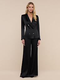 A person with long blonde hair wears the Colin Silk Charmeuse Blazer—a black silk power suit blazer styled with matching wide-leg trousers—standing against a plain white background.