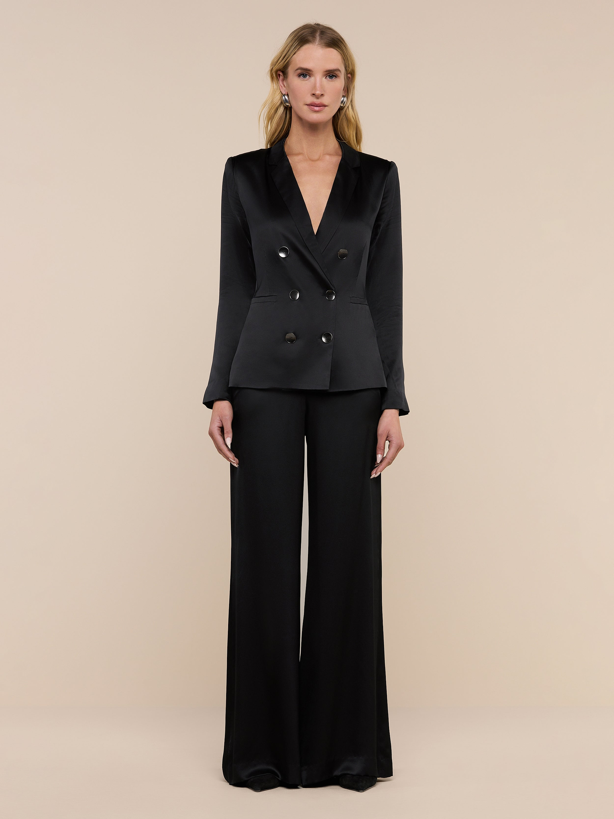 A woman stands facing forward, wearing the Colin Silk Charmeuse Blazer and wide-leg black pants against a plain white background.