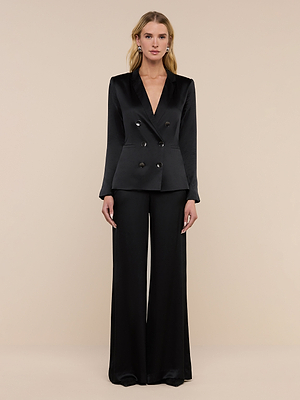 A woman stands against a plain beige background wearing the Colin Silk Charmeuse Blazer and matching wide-leg pants—a black, double-breasted power suit. She faces forward, arms relaxed at her sides.