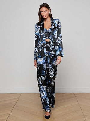 A woman stands indoors wearing the Colin Silk Blazer by L’AGENCE, styled with a matching crop top and wide-leg pants in an intricate blue and white porcelain print. She completes the look with black heels and silver earrings.