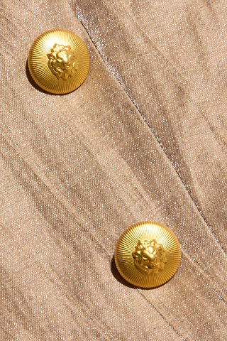 Close-up of two decorative gold lion head buttons on textured beige fabric, featured on the Inez Cropped Blazer.
