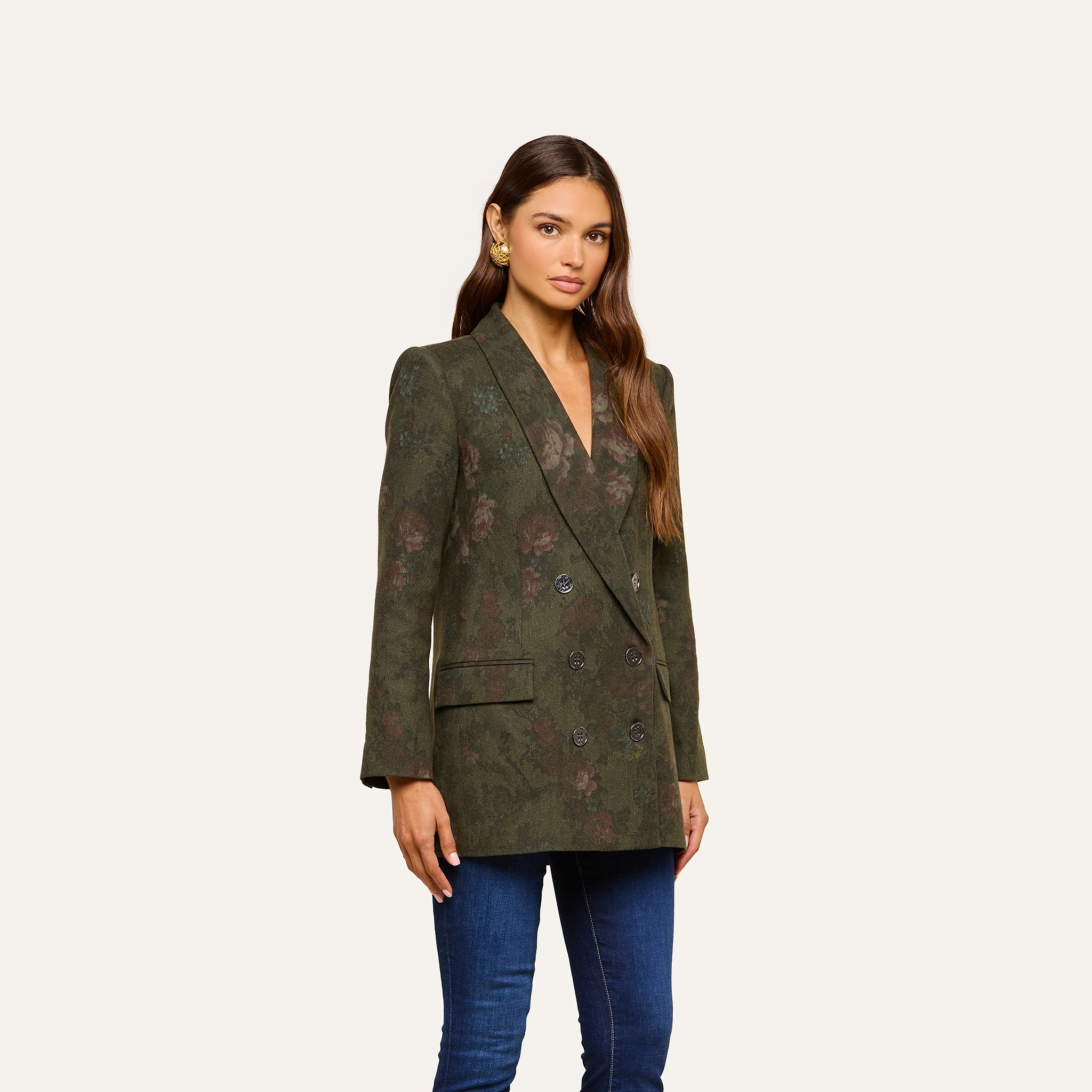 A woman wearing the oversized Jayda Blazer in a green floral print with jeans stands against a plain light background, looking at the camera with a neutral expression.