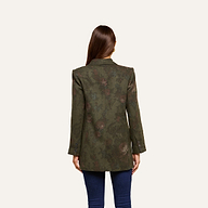 A woman with long brown hair faces away, wearing the Jayda Blazer—a dark green, floral print blazer—paired with dark blue jeans against a plain light background.