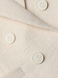 Close-up of the cream-colored, textured fabric from the Brooke Tweed Blazer, showcasing four embossed round buttons adorned with a laurel wreath and crest design.